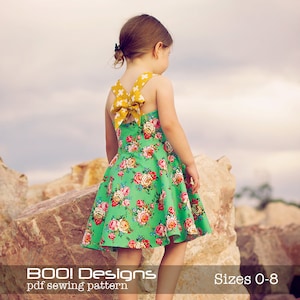 May include: A green floral dress with a yellow bow on the back. The dress has a sleeveless design and a full skirt. The dress is for sizes 0-8. "BOO! Designs" and "pdf sewing pattern" are written at the bottom of the image.