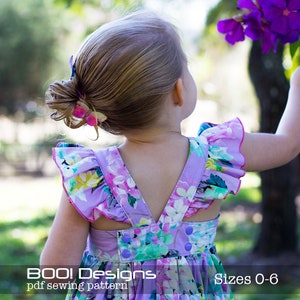 Może przedstawiać: Dziewczynka w fioletowej sukience z kwiatowym wzorem, falbankami na rękawach i dekoltem w kształcie litery V. Sukienka ma różową lamówkę i guziki z tyłu. Dziewczynka patrzy na coś poza kadrem. Na dole zdjęcia widoczny jest tekst "BOO! Designs pdf sewing pattern" i "Sizes 0-6".