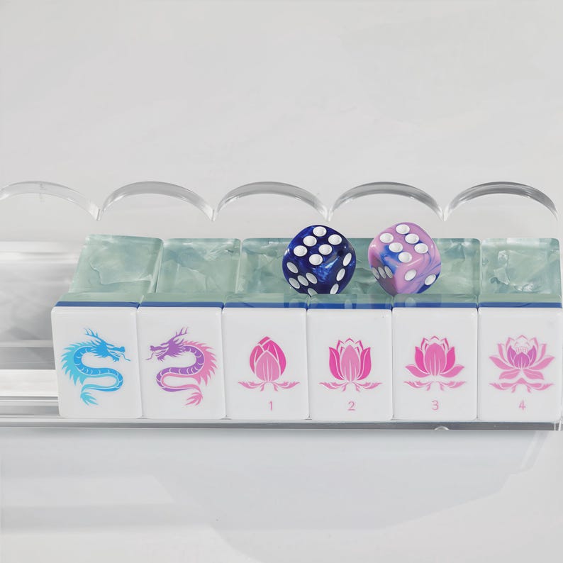 May include: A set of six white mahjong tiles arranged in a clear acrylic rack. The tiles feature blue and purple dragon illustrations and pink lotus flower designs with the numbers 1 through 4. Two six-sided dice, one blue and one purple, rest on top.