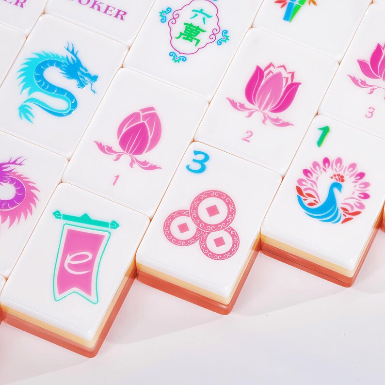 Puede incluir: Una colecci&oacute;n de fichas de mahjong rectangulares blancas con coloridos dise&ntilde;os impresos que incluyen un drag&oacute;n azul, flores de loto rosas, un pavo real, un estandarte con la letra e y tres monedas circulares con centros cuadrados, todas con bases naranjas.