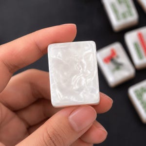 May include: A rectangular mahjong tile with a smooth, glossy white surface featuring a pearlescent, marbled texture. The tile has rounded corners and a solid, opaque appearance, presented as a single game piece with a clean, reflective finish.
