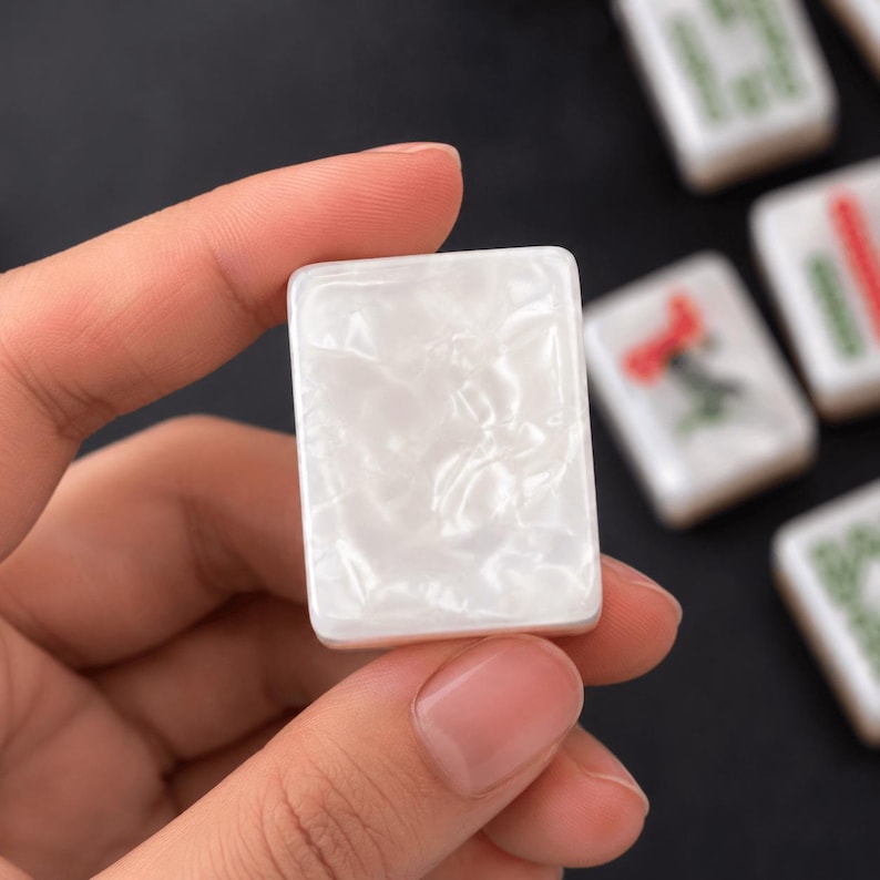 May include: A rectangular mahjong tile with a smooth, glossy white surface featuring a pearlescent, marbled texture. The tile has rounded corners and a solid, opaque appearance, presented as a single game piece with a clean, reflective finish.