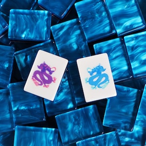 May include: A collection of rectangular mahjong tiles with a swirling blue and white marbled pattern. Two white tiles are placed on top, one featuring a purple dragon illustration and the other featuring a light blue dragon illustration.