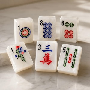 May include: Six rectangular white Mahjong tiles with a marbled finish. The tiles feature engraved symbols and numbers in black, blue, red, and green ink, including a bird illustration, Chinese characters, and circular patterns on the face of each piece.