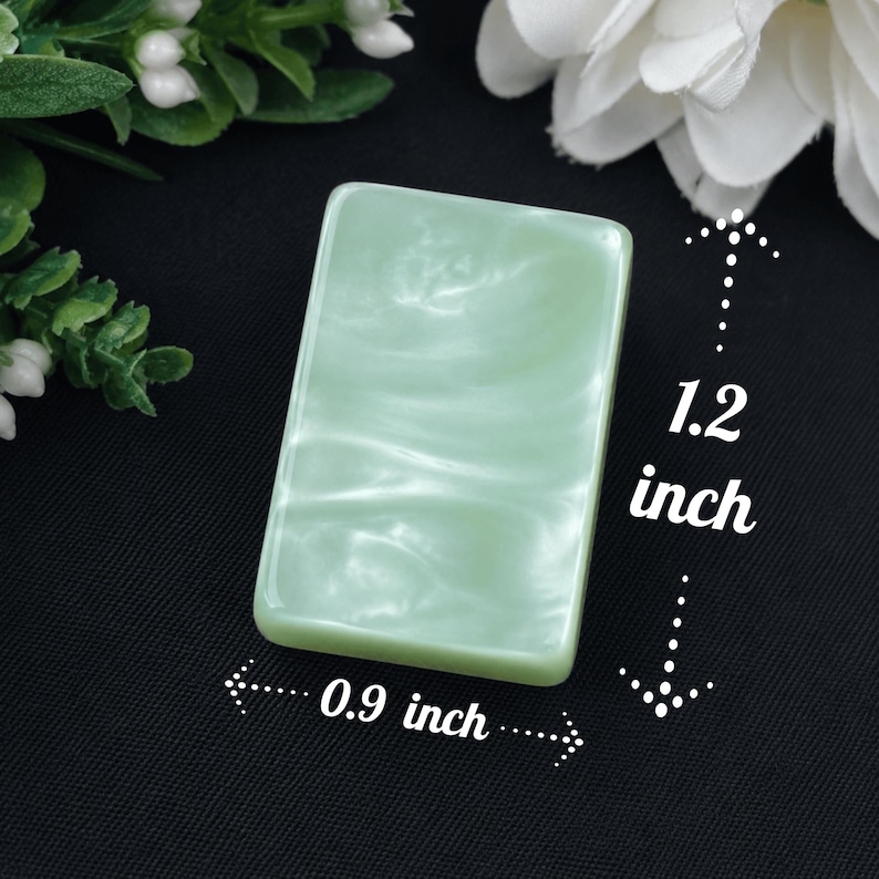 May include: A rectangular, light green, marbled resin cabochon with a smooth, glossy finish. The piece measures 1.2 inches in height and 0.9 inches in width, as indicated by the white text and arrows printed directly on the image for reference.