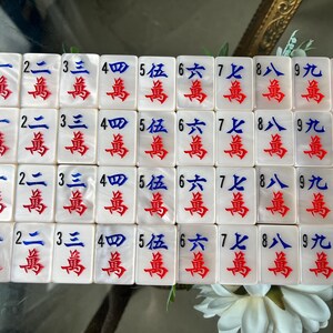 May include: A set of white rectangular Mahjong tiles arranged in a grid. Each tile features a black Arabic numeral from 1 to 9, blue Chinese characters, and red Chinese characters. The final column displays tiles with a red dragon illustration.