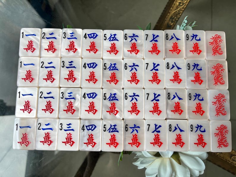 May include: A set of white rectangular Mahjong tiles arranged in a grid. Each tile features a black Arabic numeral from 1 to 9, blue Chinese characters, and red Chinese characters. The final column displays tiles with a red dragon illustration.