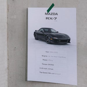 Könnte beinhalten: Ein schwarzer Mazda RX-7 (FD) ist auf einem weißen Informationsblatt abgebildet. Das Blatt enthält Angaben wie Baujahr (1992-2002), Motor (1,3L Twin-Rotor Turbo Rotary), Leistung (276 PS), Drehmoment (314 Nm) und 0-100 km/h (4,9 Sek.).