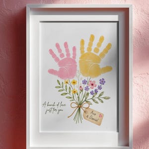 May include: A framed print featuring a pink handprint and a yellow handprint arranged to resemble a flower bouquet with green stems and small colourful flowers. The text reads A bunch of love just for you and a tag labelled Ava & Daniel.