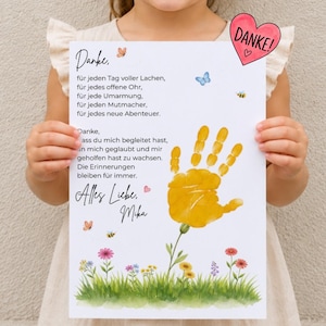 May include: A white rectangular print featuring a German poem, a yellow handprint shaped like a flower, and colourful floral illustrations at the bottom. A pink heart sticker with the word DANKE is attached to the top right corner of the paper.