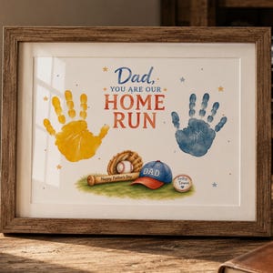 Könnte beinhalten: Gerahmtes Kunstwerk mit Baseball-Motiv. Der Druck zeigt gelbe und blaue Handabdrücke, einen Baseball, einen Schläger und eine Baseballkappe. Der Text lautet "Papa, du bist unser Home Run" und "Alles Gute zum Vatertag".