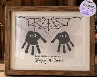 May include: A framed print featuring two gray handprints transformed into spiders hanging from a black spiderweb. The text reads, "JUST DROPPED IN TO SAY Happy Halloween." A circular sticker in the corner states, "Instant download for 1-4 children."