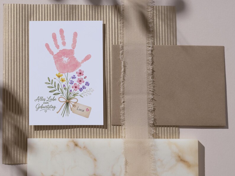 May include: A rectangular greeting card featuring a pink handprint illustration transformed into a flower blossom atop a bouquet of colourful wildflowers. The text reads Alles Liebe zum Geburtstag with a small tag labelled Luca and a heart icon.