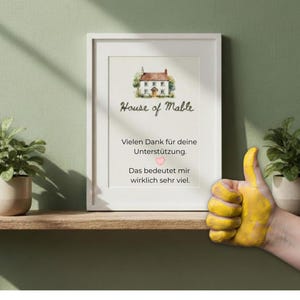 Op de afbeelding: Een ingelijste print met de tekst "House of Mable" en een aquarel illustratie van een huis. De print bevat Duitse tekst die dankbaarheid uitdrukt. Een hand met een geel geschilderde duim omhoog staat in de afbeelding.