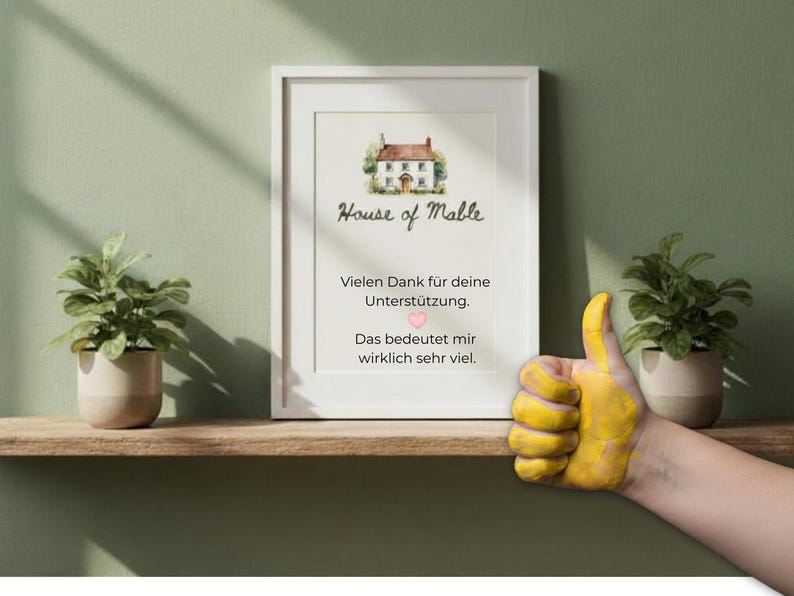 Op de afbeelding: Een ingelijste print met de tekst "House of Mable" en een aquarel illustratie van een huis. De print bevat Duitse tekst die dankbaarheid uitdrukt. Een hand met een geel geschilderde duim omhoog staat in de afbeelding.