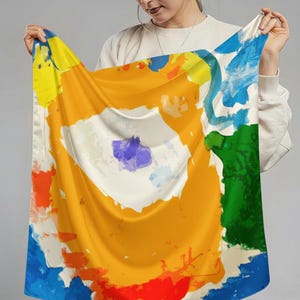 Op de afbeelding: Een vierkante zijden sjaal met een abstract ontwerp. De sjaal heeft een levendig kleurenpalet van geel, oranje, blauw, groen en wit. Het ontwerp lijkt een mix te zijn van penseelstreken en vormen, wat een moderne en artistieke uitstraling creëert.