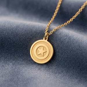 May include: A gold-colored pendant necklace featuring a circular pendant with a star design. The pendant hangs from a delicate chain, set against a blue velvet background. The necklace is a piece of jewelry.