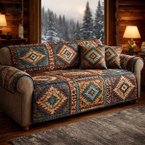 May include: A sofa with a patterned quilt and matching cushions. The quilt has a geometric design in shades of blue, brown, and gold. The sofa is set against a backdrop of a window with a snowy landscape.