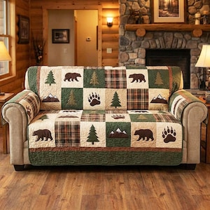 May include: A quilted sofa cover with a patchwork design featuring bears, pine trees, bear paw prints, and mountains. The color palette includes shades of green, brown, and cream, creating a rustic, outdoorsy theme. The cover is designed to fit a standard sofa.