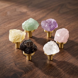 Può includere: Sei pomelli per mobili con cime in pietre grezze e irregolari di colore giallo, verde chiaro, viola, rosa, trasparente e marrone scuro, montati su una base metallica cilindrica color ottone con varie texture di pietra naturale.
