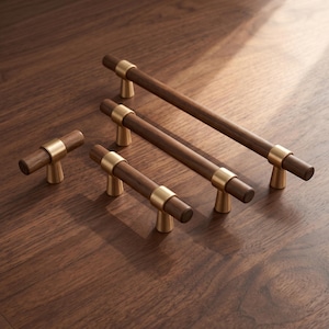 May include: A collection of four cabinet hardware pieces featuring cylindrical dark brown wood bars accented with brushed gold metal mounts. The set includes one small knob and three drawer pulls of varying lengths, all with a smooth finish.