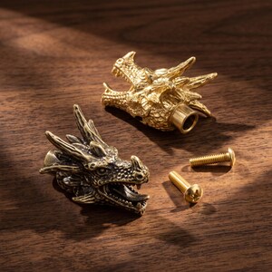 May include: Two brass-toned metal cabinet knobs shaped like detailed dragon heads with open mouths and textured scales. Each knob features a cylindrical attachment point on the back and is accompanied by a matching metal screw for installation.