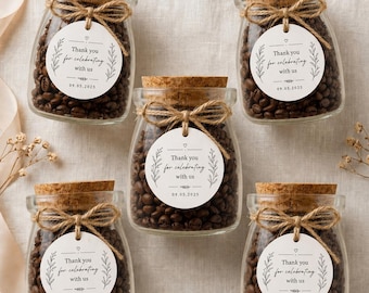 Könnte beinhalten: Fünf Gläser gefüllt mit Kaffeebohnen, jeweils mit einem Korkdeckel verschlossen und mit Bindfaden gebunden. Jedes Glas hat ein weißes Etikett mit der Aufschrift "Thank you for celebrating with us" und dem Datum 09.05.2025.