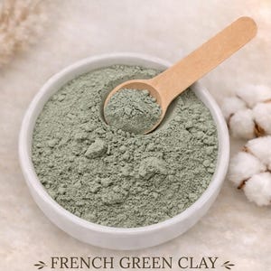 May include: A white bowl filled with green French clay, with a wooden scoop resting inside. The text "FRENCH GREEN CLAY" is displayed below, along with the words "DETOXIFYING • ABSORBENT • BALANCING".