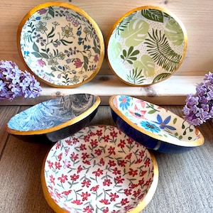 Puede incluir: Un conjunto de cuencos decorativos con estampados florales y de hojas. Los cuencos tienen bordes dorados y colores exteriores variados, incluyendo negro y azul. Los diseños interiores presentan una variedad de estampados florales y botánicos coloridos.