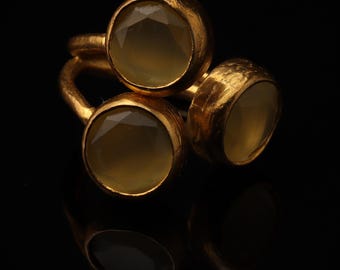 May include: A gold-toned ring featuring three round, faceted, translucent pale yellow stones set in textured metal bezels. The band is constructed from a continuous piece of metal that connects the three circular settings in a cluster arrangement.