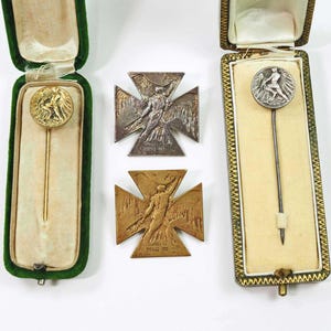 May include: An assortment of vintage pins and crosses. Two pins are displayed in their original presentation boxes. The pins have circular medallions with relief figures. Two crosses are also shown, one silver and one bronze, each with a relief figure.