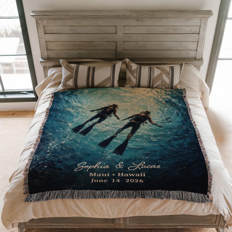 May include: A woven throw blanket featuring a vibrant underwater scene with two scuba divers. The blanket has a blue and teal color scheme, with the names "Sophia & Lucas", location, and date printed on it. The blanket has a fringed edge.