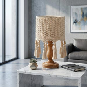 May include: A beige crochet lampshade with a wooden base and decorative tassels. The lamp sits on a marble table, with a small succulent plant and a notebook nearby. The lamp's design adds a touch of bohemian style to the room.