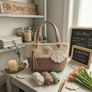 May include: A handmade crochet tote bag in cream and brown with a gold clasp and tassel. The bag features a decorative flower and is displayed with yarn, crochet hooks, and the text "HANDMADE WITH LOVE."