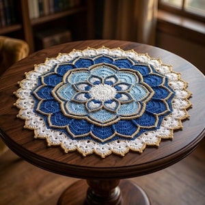 May include: A circular crochet doily featuring a layered floral mandala pattern in shades of white, light blue, and deep blue, with thin gold-colored yarn accents outlining the petals and a scalloped white border edge.