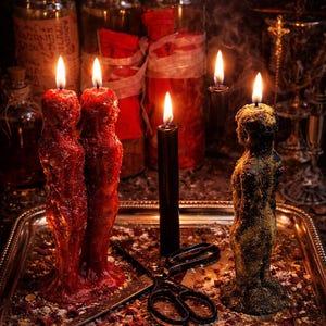 May include: Two red human-shaped candles, one black human-shaped candle with gold dust, and one thin black taper candle are lit on a silver tray. A pair of black metal scissors lies between the candles, surrounded by scattered dried herbs and petals.