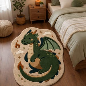 Könnte beinhalten: Ein unregelmäßig geformter Teppich mit einem Cartoon-Drachen in Dunkelgrün und Beige. Der Drache hat Flügel, einen langen Schwanz und ist von kleinen gestickten Motiven wie Wolken, Sternen und Flammen auf einem hellbeigen Hintergrund umgeben.