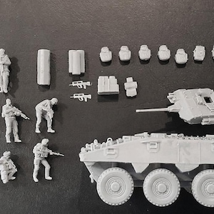 Op de afbeelding: Een verzameling ongeverfde grijze hars modelbouwset onderdelen, waaronder negen soldaatfiguren in diverse tactische houdingen, een pantservoertuigchassis met meerdere wielen, een losse koepel en een assortiment aan kleine uitrusting en wapens.