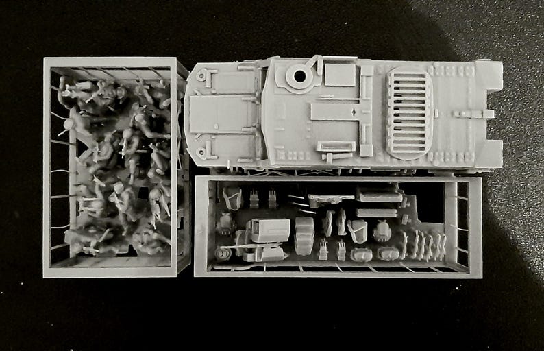 May include: A gray plastic model kit of a military vehicle, with separate compartments for soldiers and equipment. The top view shows the vehicle's details, including hatches and vents. The kit includes miniature soldiers and various accessories.