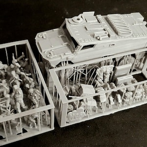 May include: A gray model of a military vehicle with detailed features, including a top hatch and side panels. The model is partially disassembled, revealing interior components and figures within a cage-like structure. The scene suggests a diorama or model kit.