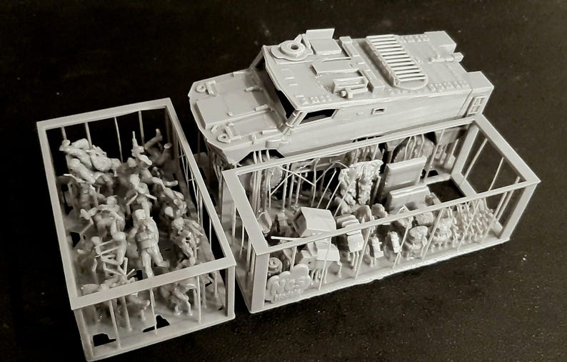 May include: A gray model of a military vehicle with detailed features, including a top hatch and side panels. The model is partially disassembled, revealing interior components and figures within a cage-like structure. The scene suggests a diorama or model kit.