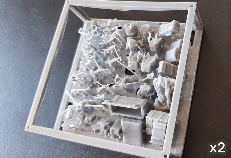 Puede incluir: Un kit de modelo de pl&aacute;stico gris con varios componentes en miniatura, incluyendo cajas, mochilas y otros elementos de tem&aacute;tica militar, se muestra dentro de un marco de pl&aacute;stico transparente. La imagen muestra dos kits id&eacute;nticos.