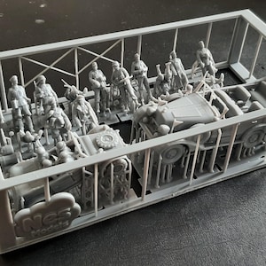 Pu&ograve; includere: Un kit di modelli in plastica grigia contenente figure e veicoli in miniatura. Il kit include diversi soldati in varie pose, insieme a un piccolo camion e altre attrezzature militari. I pezzi sono ancora attaccati al telaio.