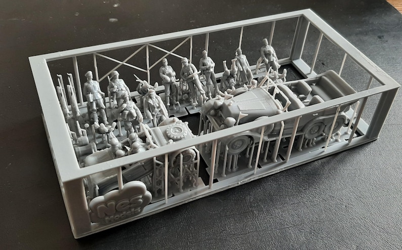 Pu&ograve; includere: Un kit di modelli in plastica grigia contenente figure e veicoli in miniatura. Il kit include diversi soldati in varie pose, insieme a un piccolo camion e altre attrezzature militari. I pezzi sono ancora attaccati al telaio.