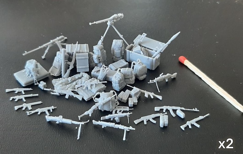 Puede incluir: Colecci&oacute;n de modelos militares grises en miniatura, que incluyen rifles, ametralladoras, mochilas, cajas y un mortero con tr&iacute;pode. Se incluye una cerilla para la escala, y el texto "x2" es visible.