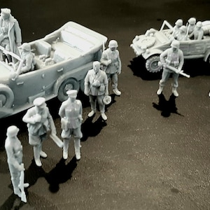 Pu&ograve; includere: Una collezione di veicoli militari e soldati in miniatura grigi. La scena comprende due auto scoperte e diversi soldati in uniforme, alcuni con fucili. I modelli sono dettagliati e sembrano essere in plastica.