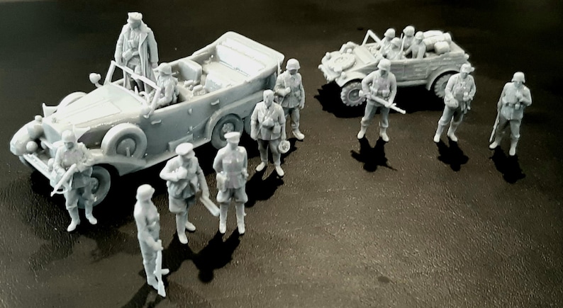 Pu&ograve; includere: Una collezione di veicoli militari e soldati in miniatura grigi. La scena comprende due auto scoperte e diversi soldati in uniforme, alcuni con fucili. I modelli sono dettagliati e sembrano essere in plastica.