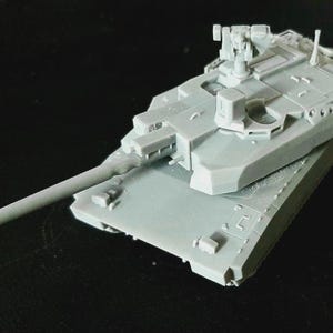 Op de afbeelding: Een lichtgrijs, onbeschilderd schaalmodel van een gevechtstank met een lange loop, een draaibare koepel met een gemonteerd machinegeweer en gedetailleerde rompbeplating. Het model is vervaardigd uit een eenkleurig harsmateriaal.