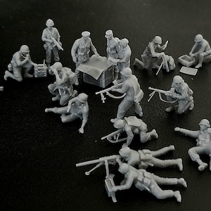 Op de afbeelding: Een verzameling ongeverfde miniatuur militaire figuren in verschillende poses, waaronder knielende soldaten, die met geweren richten en machinegeweren bedienen. De figuren zijn grijs en lijken van plastic of hars te zijn.