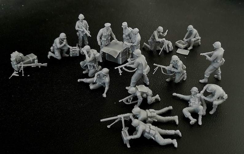 Op de afbeelding: Een verzameling ongeverfde miniatuur militaire figuren in verschillende poses, waaronder knielende soldaten, die met geweren richten en machinegeweren bedienen. De figuren zijn grijs en lijken van plastic of hars te zijn.